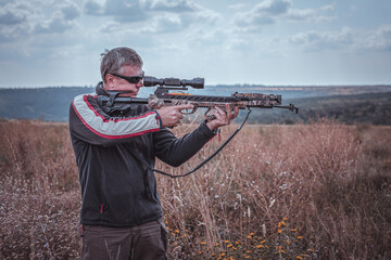Hunter with a crossbow takes aim, half-length plan on the background of nature
