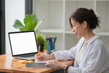 Beautiful Asian businesswoman sitting in an office chair holding pencils notebooks and tablet place at the table.