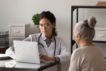 Serious young female doctor meeting with elderly patient in office, listening to woman health...