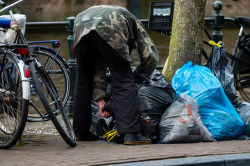 A man searches for deposit bottles in garbage bags along a canal in Amsterdam, Noord-Holland province, The Netherlands