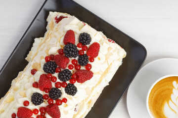 Closeup homemade delicious meringue dessert with berries and cup of coffee cappuccino on white wooden table. Top view.