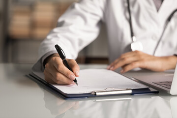 Hands of general practitioner filling paper medical records. Doctor in white coat doing paperwork...