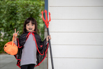 Asian child girl in demon costume holding black and red trident, Happy halloween concept