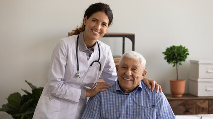 Fototapeta premium Head shot portrait of optimistic young female therapist and happy older patient. Senior man visiting doctor, looking at camera, smiling, staying healthy due to good treatment, geriatric medic care