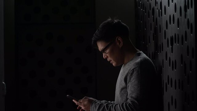 sad young asian man sitting on the floor checking mobile phone with bad news message in the dark at home he lost job in quarantine