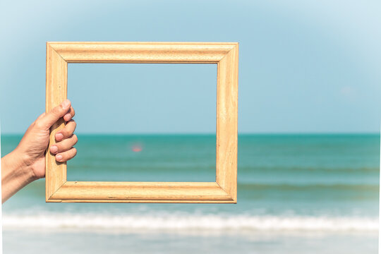 hand holding Wooden  frame empty blank photo with view of blue sky, on blur nature sea  background