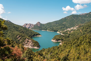 Fototapeta na wymiar The dam wall at Lac de Tolla in Corsica surrounded by rocky cliffs and pine forest with mountains in the distance