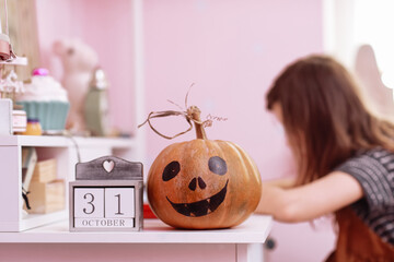 Halloween pumpkin and calendar with 31 october on wooden table in schoolgirls room. child girl on backgroung doing homework