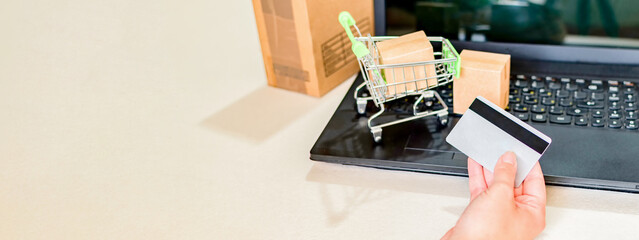 Woman hand with credit card, boxes with a shopping cart or trolley near a laptop keyboard.
