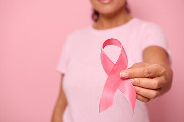 Close-up of female adult hand holding pink ribbon. World Cancer Day. Breast and abdominal cancer awareness, October Pink day on colored background, copy space. Breast cancer support concept.