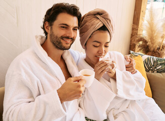 Loving young couple in white bathrobes spending a weekend at a spa and enjoying wellness tea. Resort and spa salon