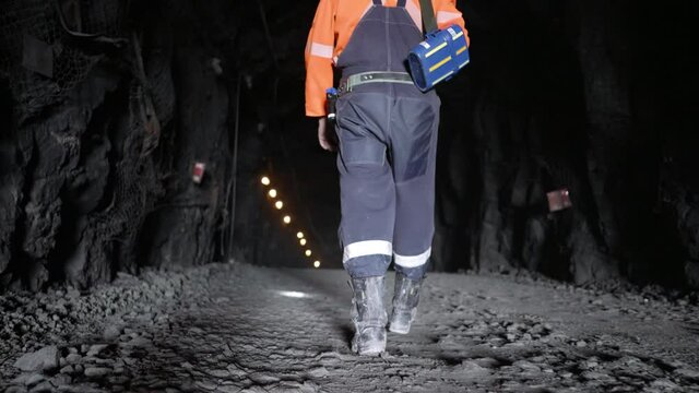 A miner in reflective clothing walking through an underground mine.