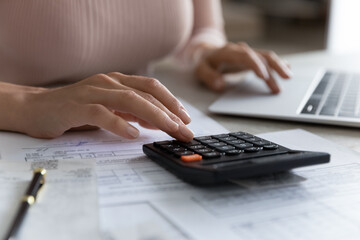 Close up young woman using calculator, summarizing utility bills, managing household budget, planning domestic savings or investments, financial accounting using e-banking application concept.