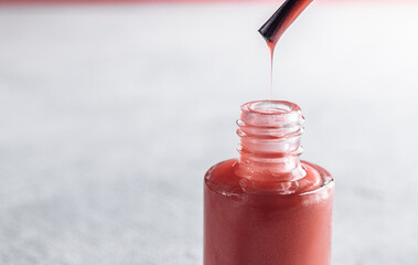 pink nail polish up close. from the brush, the varnish drips into a jar in macro