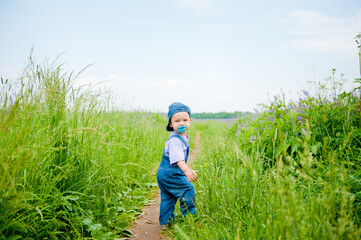 a pretty little boy walks through a field with flowers daisies and sage in the village