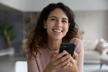 Fototapeta na wymiar Head shot portrait laughing happy young hispanic woman holding cellphone, looking at camera. Addicted to modern technology sincere millennial female user involved in playing games or shopping online.