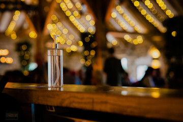 A bottle of hand sanitiser (no label or logos) on a bench with copy space and out of focus elements/lighting