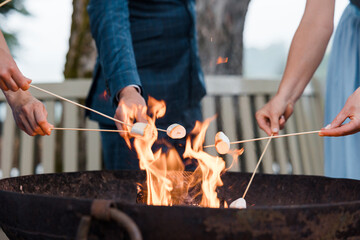 Fototapeta premium People cooking marshmallows on sticks over a flaming fire pit (no visible faces)