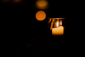 Single lit candle in glass container with warm light and out of focus background