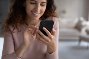 Focus on smartphone in female hands, smiling millennial latin woman using cellphone software applications, typing message or responding email, playing game or shopping online in internet store.