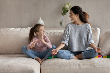 Pleasant beautiful young hispanic mother sitting on cozy sofa in lotus position with adorable...