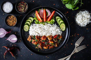 Roast pork  with jasmine rice and vegetables served on black plate on wooden table