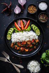 Roast pork  with jasmine rice and vegetables served on black plate on wooden table