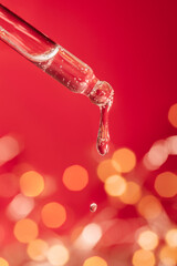 Pipette with serum on a red holiday background with bokeh.