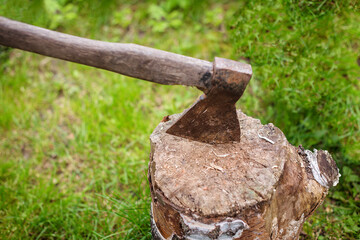 Old ax with a wooden handle stucking into a tree stump. Blurred background, sunlight effect