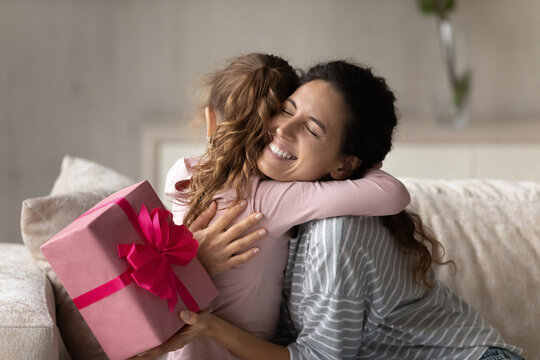 Emotional happy young mother feeling thankful getting surprise gift, cuddling little preschool kid daughter, celebrating birthday or special event together at home, joyful family sincere relations.