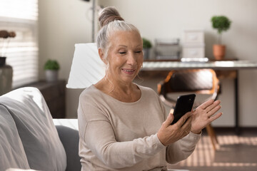 Happy elderly grey haired lady using smartphone at home, making video call, talking to family, relatives online. Senior patient consulting doctor at virtual meeting on mobile phone, smiling at screen