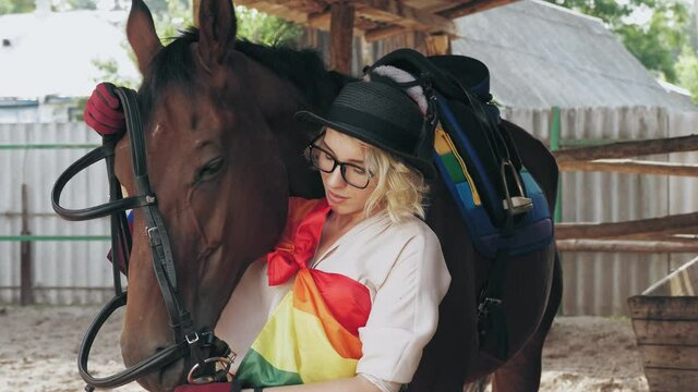 lgbt rainbow flag. horse care. equestrian sport hobby. a rider girl, with lgbt rainbow symbols, puts on bridle, reins on her horse. Bisexual, transgender or lesbian woman.
