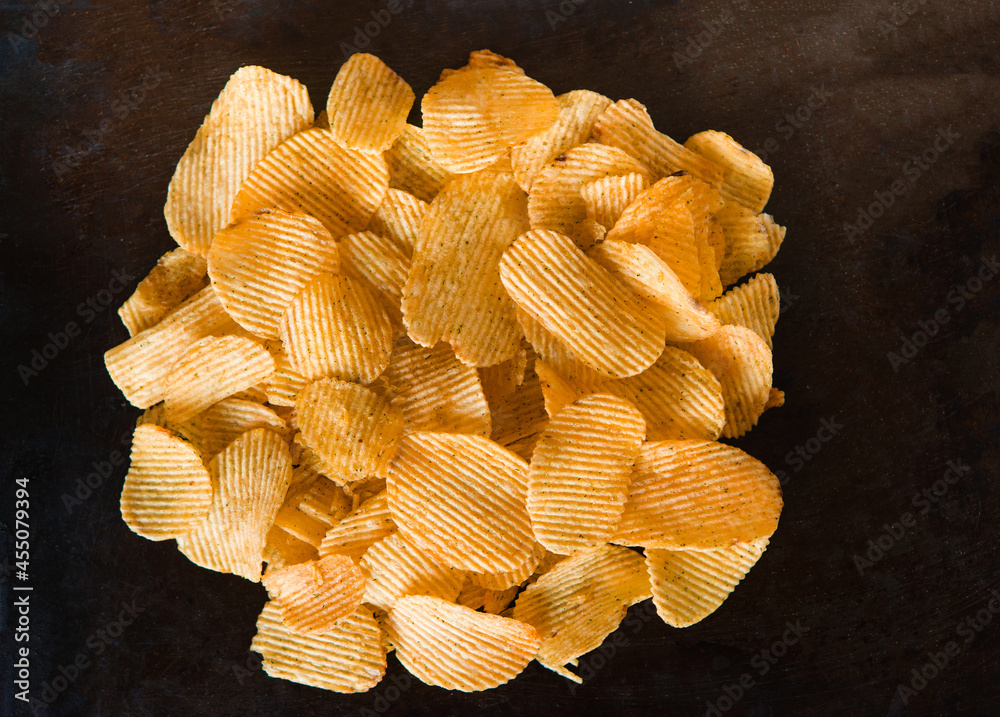 Poster Crispy potato chips in a plate on metallic black grunge background