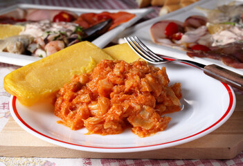 Delizioso piatto con polenta gialla e baccalà in umido, disposto su un tavolo apparecchiato per la cena.