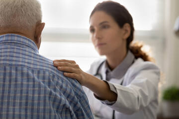 Serious GP doctor giving support to elderly 80s patient after telling bad news, holding, touching...