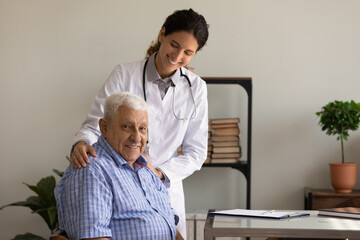 Fototapeta premium Portrait of happy female GP doctor giving hope, support, hug to senior 80s male patient, touching shoulder. Smiling senior man visiting therapist, looking at camera. Geriatric healthcare. Head shot