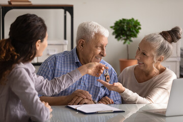 Happy retired couple of clients buying new house, receiving keys from realtor, property seller. Smiling senior husband and wife ready to move into new apartment, meeting with , real estate agent