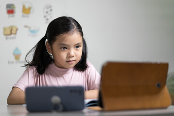 Asian child student or kid girl smiling learn from home school or people study online on computer tablet and video call learning on smartphone with happy enjoy to vocabulary english words in classroom