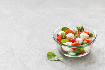 Fototapeta na wymiar Italian salad of tomatoes, onions, spinach with mozzarella in a glass bowl on a light gray background copy space