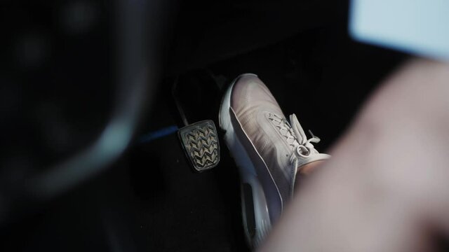 Foot in sneaker pressing gas pedal in car, close-up view.