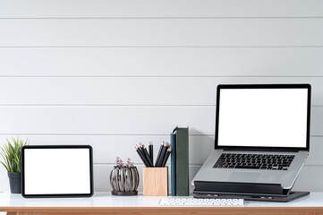Blank screen tablet and laptop computer in minimal office room with decorations and copy space.
