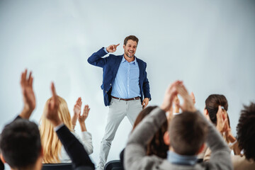 Smiling motivational speaker standing in front of his audience who is clapping. - obrazy, fototapety, plakaty