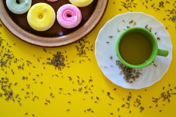 Cup of tea and colorful meringues surrounded by lavender flowers on a yellow background