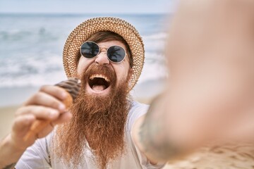 Young redhead man eating ice cream make selfie by the camera at the beach.