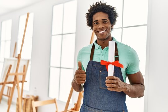 Young african american artist man holding diploma at art studio.