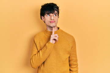 Fototapeta premium Handsome hipster young man wearing casual yellow sweater thinking concentrated about doubt with finger on chin and looking up wondering