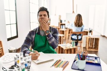Young artist man at art studio bored yawning tired covering mouth with hand. restless and...