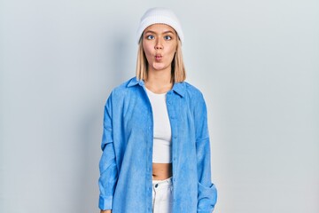 Fototapeta premium Beautiful blonde woman wearing wool hat making fish face with lips, crazy and comical gesture. funny expression.