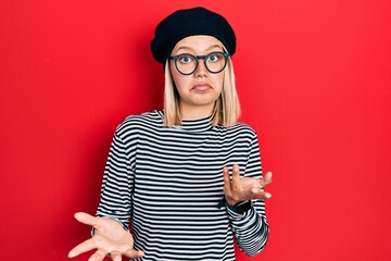 Beautiful blonde woman wearing french look with beret an glasses clueless and confused expression...