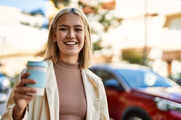 Young blonde girl smiling happy drinking take away coffee at the city.